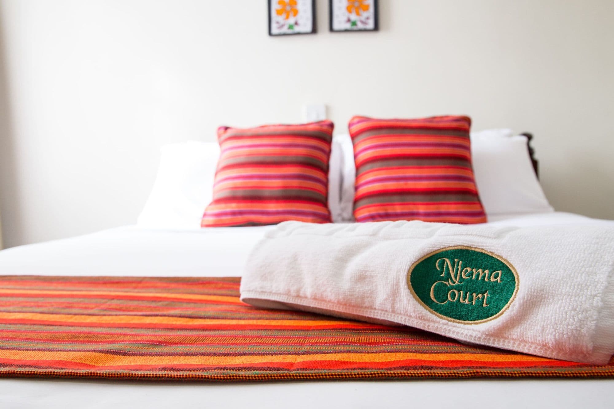 A made bed with a Njema Court embroidered towel and red striped cushions