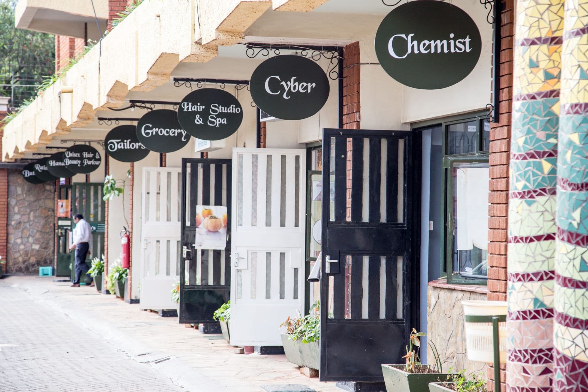 The shop arcade at Njema Court with signs for a chemist, cyber café, grocery, tailor and hair studio