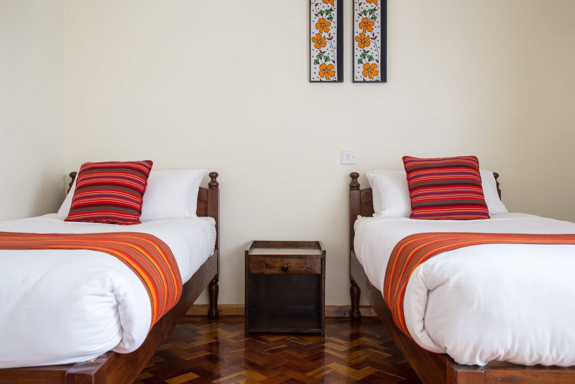 A twin bedroom with two single beds, red cushions and framed African prints